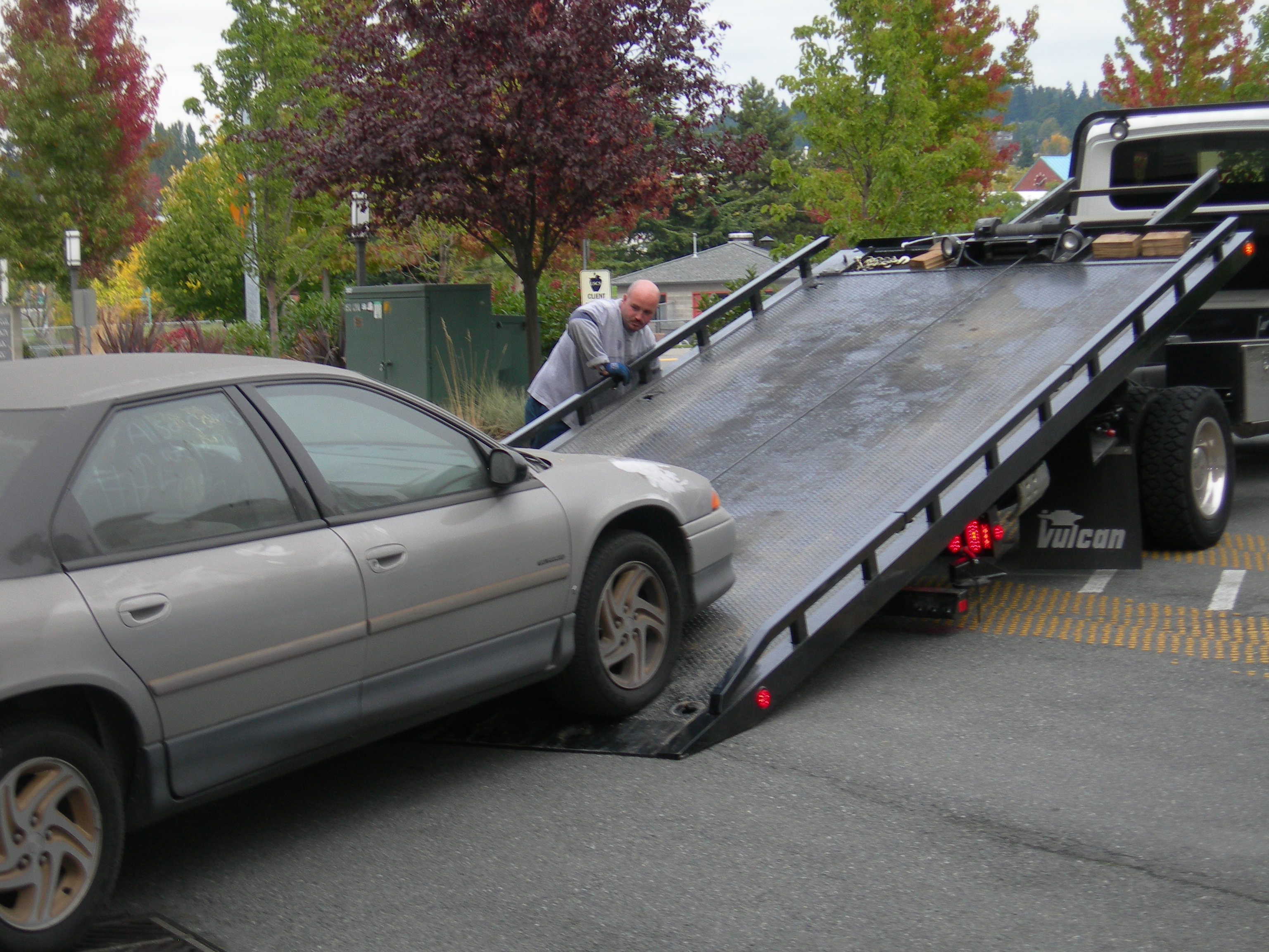 Flatbed tow truck operator loading a sedan onto the ramp